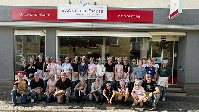 25 Konfis, Bäcker Gerd Laun, Gemeindepädagogin Johanna Krestan und Pfrin. Olivia Rahmsdorf vor der Bäckerei Preis